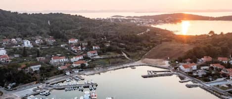 An aerial view of a coastal town with a marina, houses, and a sunset over the water.