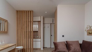 A modern room with a wooden partition, a desk with a chair, a sofa, and a kitchen area in the background. - One Bedroom Suite with Sea View and Balcony (305) (Dobra voda)