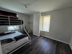A room with a bunk bed, a radiator, a window with blinds, and a ceiling light fixture.