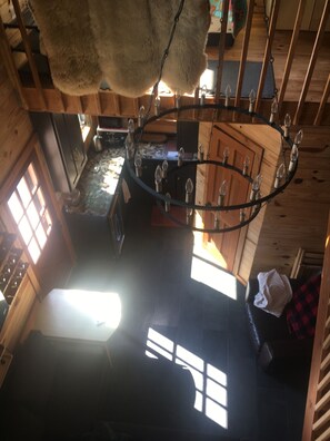 A rustic interior with a chandelier, wooden beams, and a view of the outside.