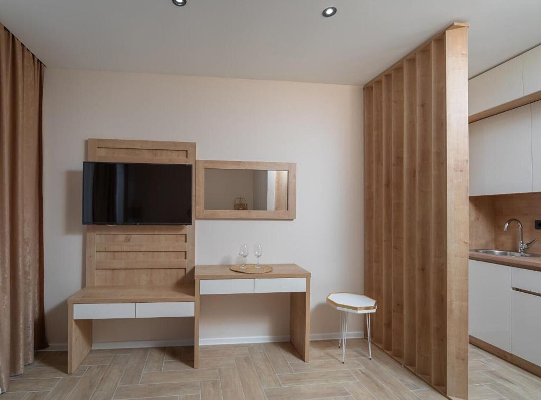 A compact room with a wooden desk, a small stool, a television, and a mirror.
