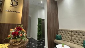 Un área de recepción con un cartel de Hotel D'Iman, un mostrador de recepción, un sofá y una planta colgada en la pared.
