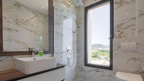 Un baño moderno con ducha de mármol, un ventanal amplio y un inodoro.