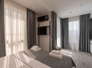 A modern hotel room with a large bed, a flat-screen TV mounted on the wall, and a small table with a cup and saucer.