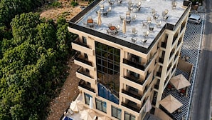 Ein mehrstöckiges Hotel mit Dachterrasse, Außenpool und mehreren Balkonen.
