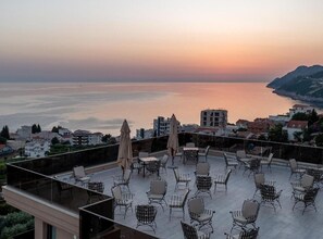 A rooftop terrace with outdoor seating and a view of the sea at sunset. - Classic Triple Room with Sea View and Balcony (403) (Dobra voda)