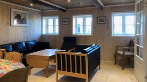 A room with wooden walls, a black leather sofa, a wooden table, and two windows. - 4 Star Holiday Home in Rudkobing (Rudkobing)