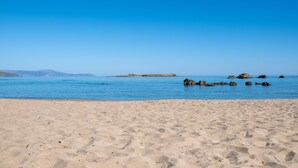 A sandy beach with calm water and distant rocky outcrops. - Feta Breeze | 60sec Walk to Nea Chora Beach (Chania)
