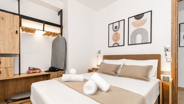 A hotel room with a bed, wooden furniture, a mirror, and artwork on the walls. - Feta Breeze | 60sec Walk to Nea Chora Beach (Chania)