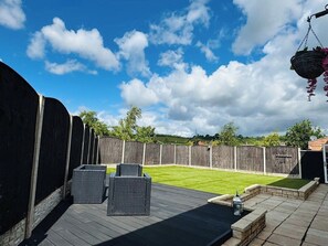Ein Garten mit Holzzaun, Rasenfläche und einer Terrassenanlage mit zwei Korbstühlen und einer Laterne.