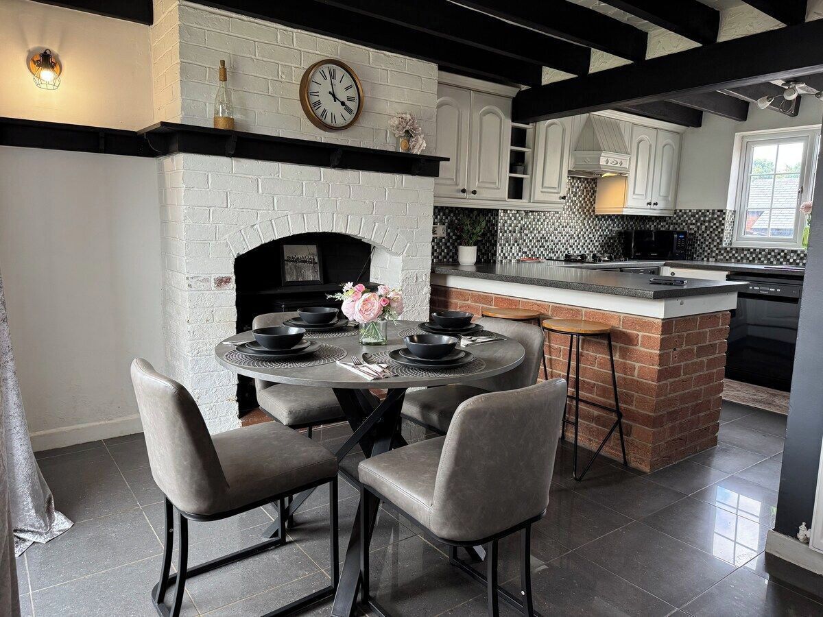A kitchen with a brick fireplace, white cabinets, a round dining table with chairs, and a small island with a sink.