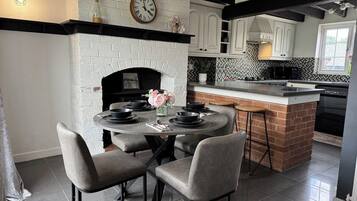 A kitchen with a brick fireplace, white cabinets, a round dining table with chairs, and a small island with a sink.
