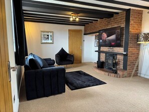 Ein Wohnzimmer mit Kamin, Fernseher und einem schwarzen Sofa.