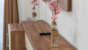 Un mueble bajo de madera para el televisor, un televisor de pantalla plana montado en la pared, un florero con flores y un control remoto.