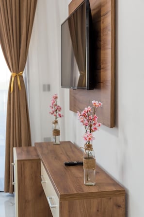 A wooden TV stand with a flat-screen TV mounted on the wall, a vase with flowers, and a remote control. - Vila Romansa (Sutomore)