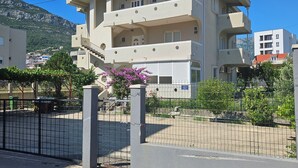 Un edificio de varios pisos con balcones, un estacionamiento cerrado y una montaña al fondo.
