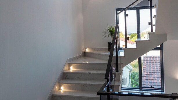 Una escalera moderna con barandas de vidrio, peldaños de mármol y vistas al exterior.
