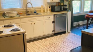 Une cuisine compacte équipée d’une cuisinière, d’un évier et d’un four à micro-ondes. On y trouve également un petit réfrigérateur et un coin repas avec une table et des chaises.