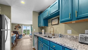 Una cocina con gabinetes azul verdoso, encimeras de granito y un refrigerador de acero inoxidable.