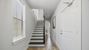 Un couloir avec un escalier, des murs blancs et une porte.