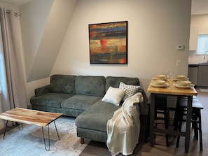 Uma sala de estar moderna com um sofá seccional, uma mesa de centro de madeira, uma mesa de jantar com cadeiras e um quadro na parede.