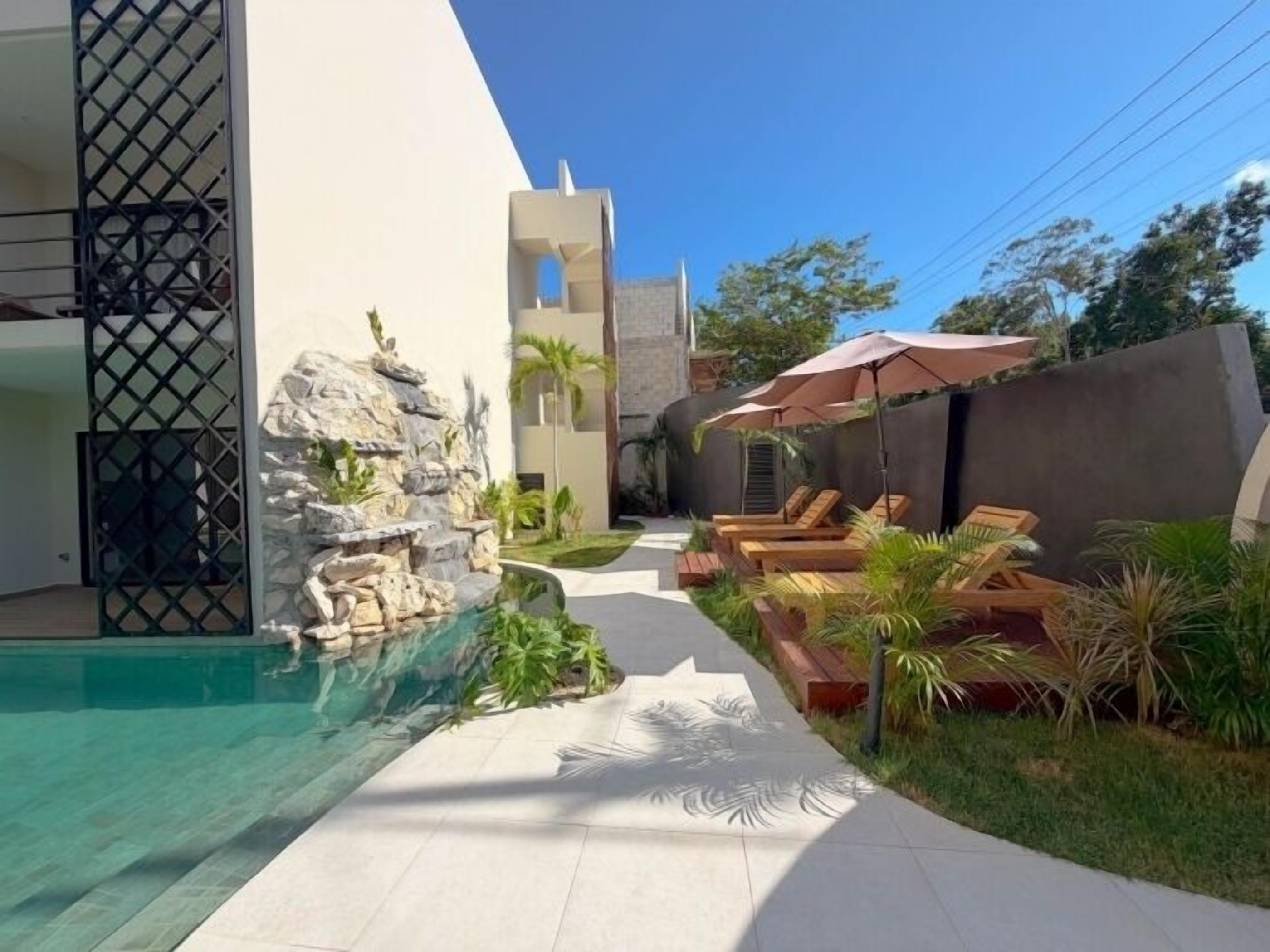 A pool area with lounge chairs, a rock feature, and a pathway.