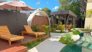 Un espace piscine extérieur moderne, doté de chaises longues en bois, d’un espace salon couvert et de bords de piscine aux lignes courbes.