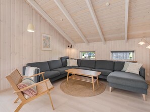 Ein modernes Interieur mit Holzboden, einem grauen Ecksofa, einem Holztisch und einem Webteppich.
