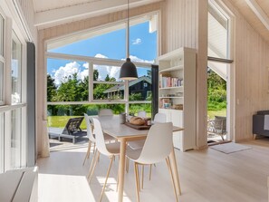 Ein modernes Interieur mit einem großen Esstisch, weißen Stühlen, einer schwarzen Pendelleuchte und einem Bücherregal.