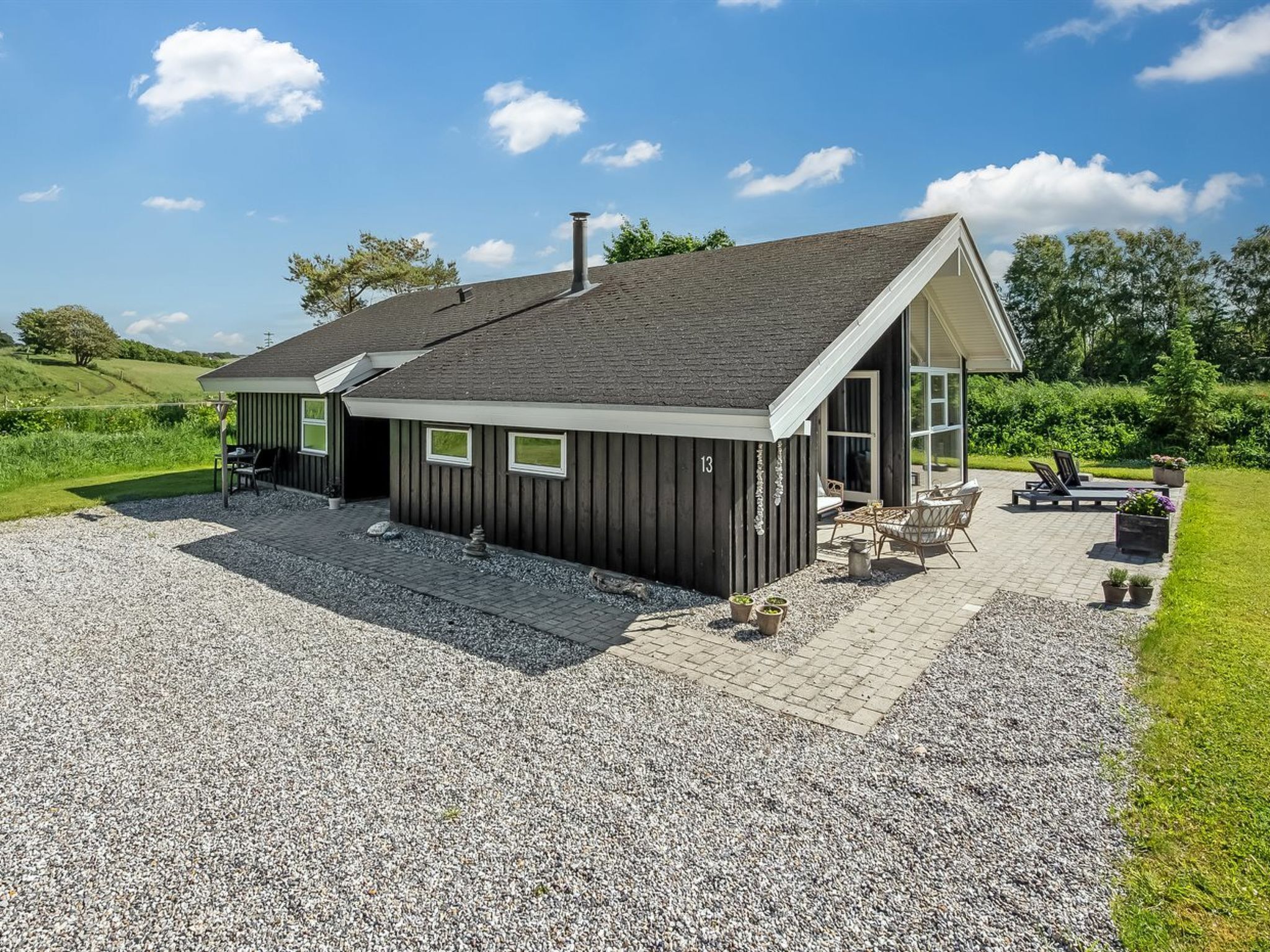 Een gelijkvloers huis met een grindpad, een terras met tuinmeubilair en een groot raam.