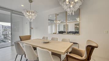 Un comedor moderno con una mesa de madera y sillas tapizadas, una araña y un espejo grande sobre la mesa.