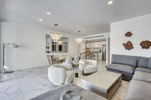 A modern living room with a marble floor, a grey sofa, a coffee table, and a dining area with chairs and a chandelier. - Spacious Luxury Apartment With Ocean Views, Pool and Steps to Playa El Médano (Cabo San Lucas)