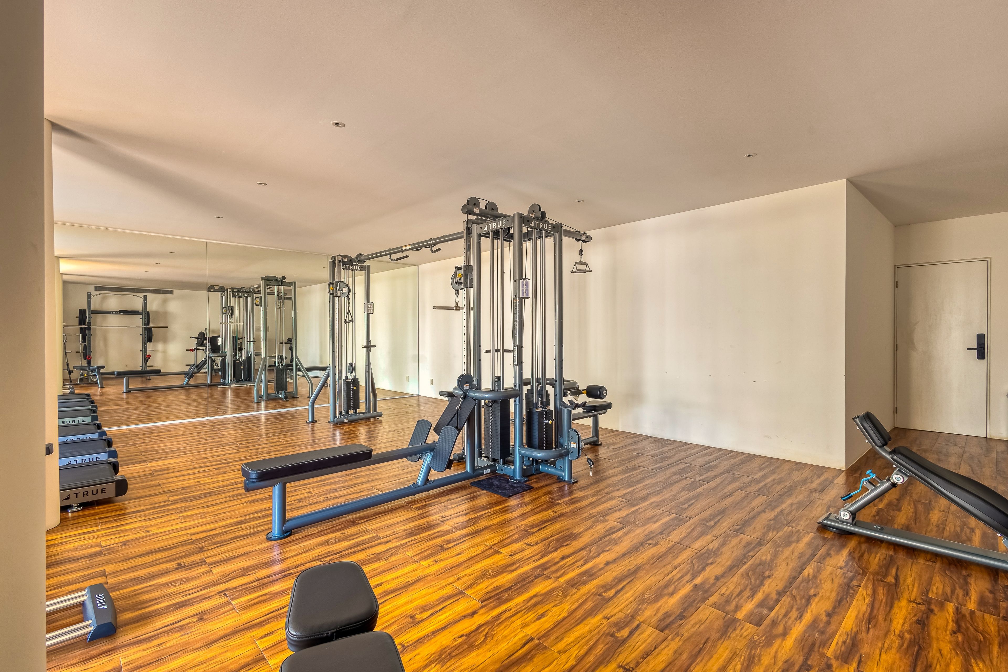 Ein Fitnessraum mit Trainingsgeräten, Holzboden und einer Bank.