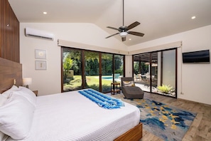 A bedroom with a bed, a ceiling fan, a large window, and a view of a pool and garden. - Casa Pochote | Private Saltwater Pool & Golf Retreat in Hacienda Pinilla (Tamarindo)