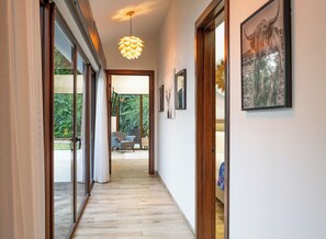 A hallway with sliding glass doors leading to an outdoor area, a pendant light, and framed artwork on the walls. - Casa Pochote | Private Saltwater Pool & Golf Retreat in Hacienda Pinilla (Tamarindo)