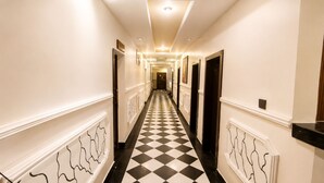 Un couloir d’hôtel avec un sol à carreaux, des murs blancs et des portes de part et d’autre.