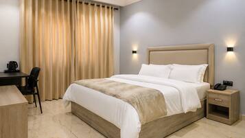 A hotel room with a bed, bedside table, lamp, desk, chair, and curtains.