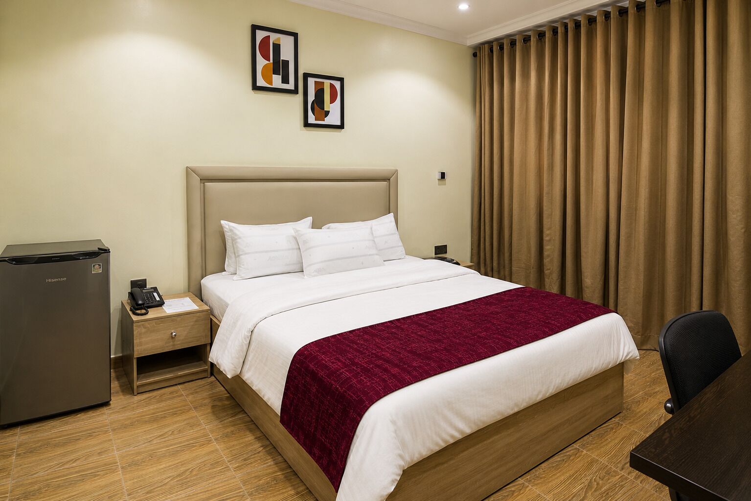 Een hotelkamer met een bed, een bureau, een koelkast en twee ingelijste foto's aan de muur.