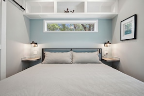 Une chambre à coucher comprenant un lit, deux tables de chevet, une fenêtre et des lampes fixées au mur.