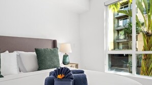 Une chambre d’hôtel avec un lit, des oreillers, une lampe et une vue sur un immeuble doté de balcons.