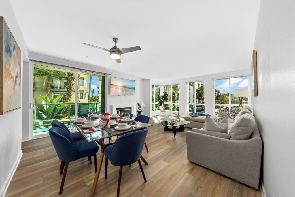 A modern living room with a dining area, large windows, and a ceiling fan.