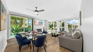 A modern living room with a dining area, large windows, and a ceiling fan.