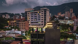 A multi-story building with a modern design, featuring a mix of glass and concrete facades, and surrounded by other buildings and greenery. - Aman Luxury 23 Bedroom 3 Pool (Medellín)