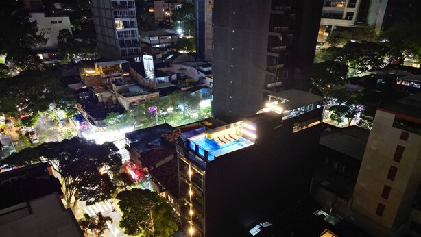 A high-rise building with multiple floors, a rooftop pool, and surrounding urban area at night. - Aman Luxury 23 Bedroom 3 Pool (Medellín)