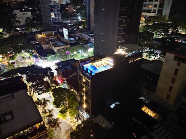 A high-rise building with multiple floors, a rooftop pool, and surrounding urban area at night. - Aman Luxury 23 Bedroom 3 Pool (Medellín)