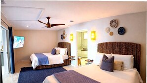 Habitación de hotel con dos camas, ventilador de techo, apliques de pared y una televisión.