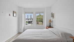 A bedroom with a bed, two windows, a nightstand, and a lamp. - Crystal Mall Room 101 in Burnaby Metrotown Area near Skytrain and Shopping. (Burnaby)