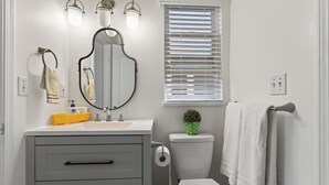 A bathroom with a toilet, sink, mirror, towel rack, and a window with blinds. - Crystal Mall Room 101 in Burnaby Metrotown Area near Skytrain and Shopping. (Burnaby)