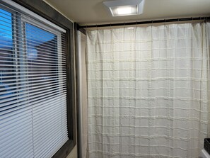 A bathroom with a window with blinds, a shower curtain, and a ceiling light.