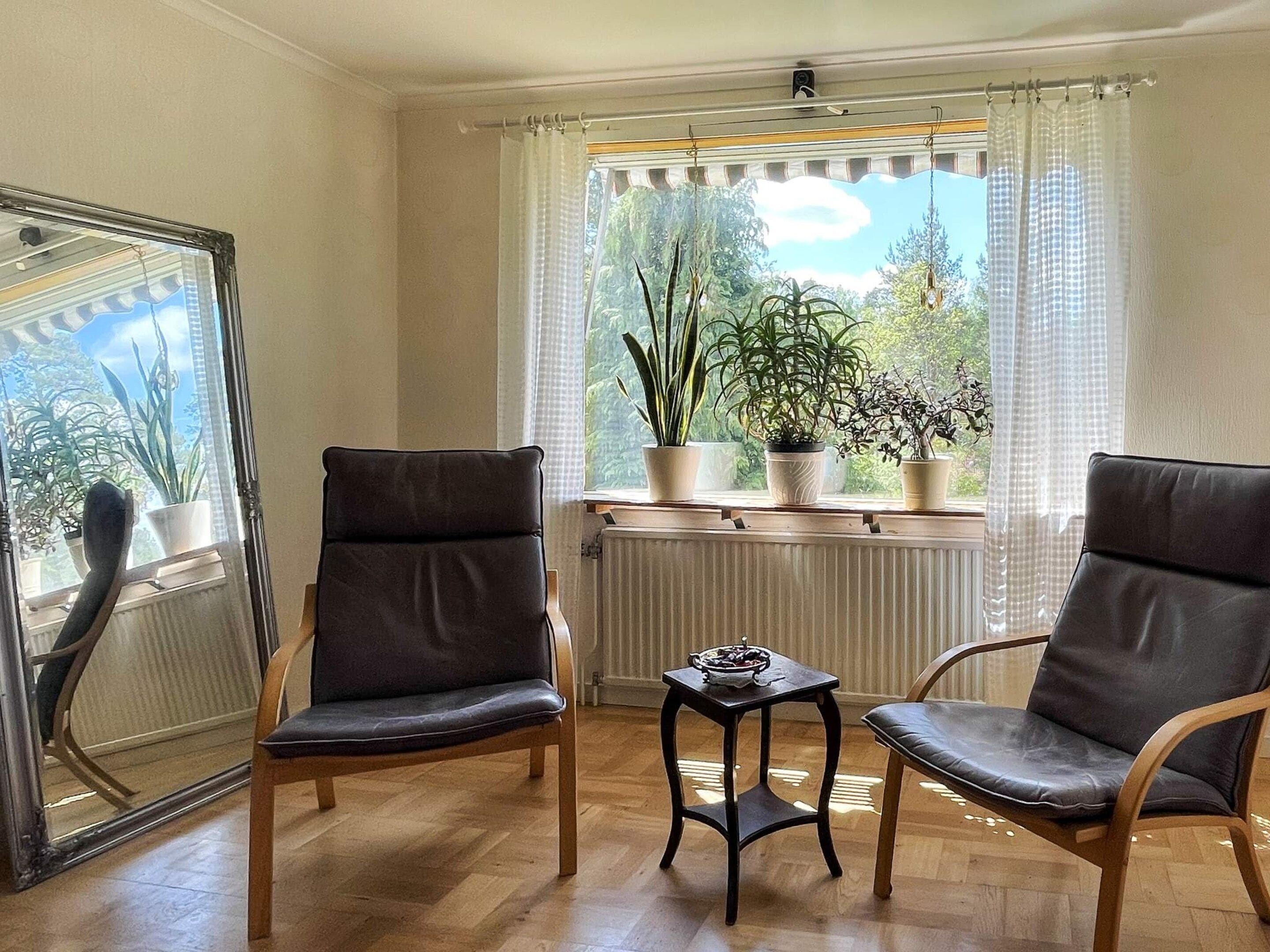 A room with two leather chairs, a small table, and a window with plants.